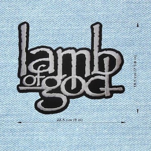 May include: Black and white embroidered patch with the text "Lamb of God". The patch is 9 inches wide and 7.58 inches tall. The text is in a stylized font with a black background and a white outline. The patch is on a light blue denim background.