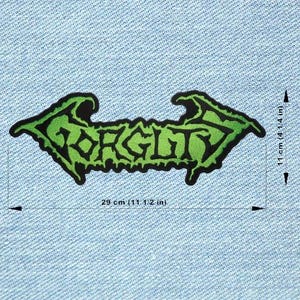 Peut inclure: Un écusson vert et noir avec le mot "FORGITY" dans une police stylisée. L'écusson en forme de flèche mesure 29 cm de long et 11 cm de haut. L'écusson est sur un fond en denim bleu clair.