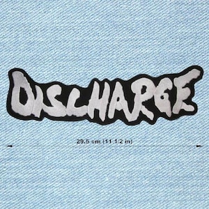 Op de afbeelding: Een zwart-wit geborduurde patch met het woord "DISCHARGE" in een gestileerd lettertype. De patch is ongeveer 29,5 cm lang en is geplaatst tegen een lichtblauwe denim achtergrond.