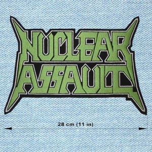 Op de afbeelding: Een groen en zwart geborduurd embleem met de woorden "NUCLEAR ASSAULT" in een gestileerd lettertype. De patch is 28 cm breed en is geplaatst tegen een lichtblauwe denim achtergrond.