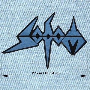Peut inclure: Un écusson bleu et noir avec le mot "Sodom" dans une police stylisée. La largeur de l'écusson est de 27 cm (10 3/4 pouces). L'écusson est sur un fond en denim bleu clair.