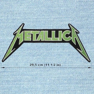 Może przedstawiać: Zielona i czarna naszywka z logo Metalliki, z napisem "METALLICA" w zielonych literach. Naszywka ma 29,5 cm długości i jest umieszczona na jasnoniebieskim tle z dżinsu.