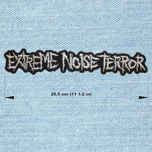 Peut inclure: Un écusson brodé noir et blanc avec le texte "EXTREME NOISE TERROR". Le patch mesure 29,5 cm de long et est affiché sur un fond en denim bleu clair. Le texte est dans une police gothique stylisée.