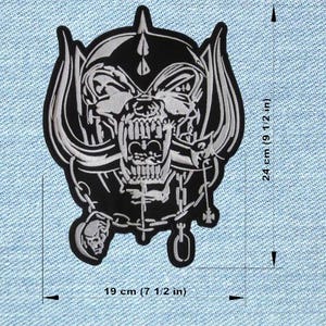 Pode incluir: Patch bordado em preto e branco com um design de caveira, correntes e um capacete com chifres. O patch mede 19 cm de largura e 24 cm de altura. O patch está em um fundo de ganga.