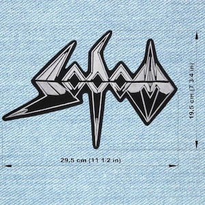 Peut inclure: Un écusson noir et argenté avec un motif géométrique, mesurant 29,5 cm de large et 19,5 cm de haut. L'écusson est sur un fond en denim bleu clair. L'écusson a un design angulaire et pointu.