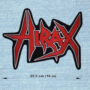 Peut inclure: Un écusson noir avec le mot "Atrax" en rouge, souligné de blanc. L'écusson mesure 25,5 cm de large et est posé sur un fond en denim bleu clair. Le texte a un design angulaire et pointu.