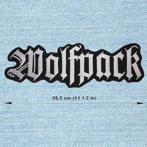 Op de afbeelding: Een zwart-wit geborduurde patch met het woord "Wolfpack" in een gotisch lettertype. De patch is 29,5 cm lang en is geplaatst op een lichtblauwe denim achtergrond.