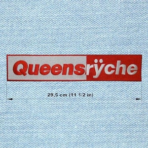Może przedstawiać: Prostokątna naszywka z napisem "Queensrÿche" w czerwonych literach na białym i czerwonym tle. Naszywka ma długość 29,5 cm (11 1/2 cala). Naszywka jest na tle jasnoniebieskiego dżinsu.