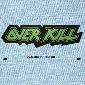 Peut inclure: Un écusson noir avec l'inscription "OVER KILL" en vert, bordée de noir. La taille de l'écusson est de 29,5 cm. Le texte est dans une police de caractères stylisée et angulaire. L'écusson est posé sur un fond en denim bleu clair.