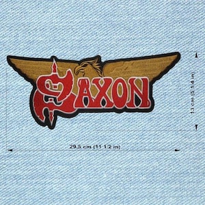 Peut inclure: Un écusson avec le mot "AXON" en rouge, bordé de noir, et un motif stylisé d'aigle et d'ailes. L'écusson mesure 29,5 cm de large et 13 cm de haut. L'écusson est sur un fond en jean.