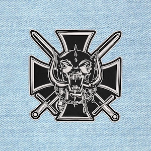 Op de afbeelding: Een zwart-witte geborduurde patch met een centrale schedel met hoorns, een helm met stekels en een ketting om de nek. De schedel is geplaatst over een zwart kruis en twee gekruiste zwaarden, alles op een achtergrond van lichtblauwe denimstof.