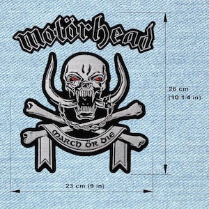 May include: Embroidered patch with the band name "Motörhead" above a skull with horns and red eyes, crossed bones, and a banner reading "March Ör Die." The patch is 26 cm (10 1/4 in) tall and 23 cm (9 in) wide.