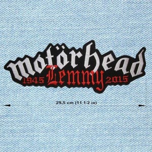 Könnte beinhalten: Ein schwarz-weiß gestickter Aufnäher mit dem Text "Motörhead Lemmy 1945-2015". Der Aufnäher ist ca. 29,5 cm lang und befindet sich auf einem hellblauen Jeansstoff.