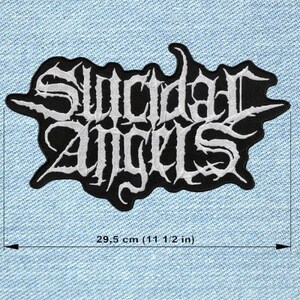 Peut inclure: Écusson brodé noir et blanc avec le texte "Suicidal Angels" en police gothique. La largeur de l'écusson est d'environ 29,5 cm. L'écusson est posé sur un fond en denim bleu clair.