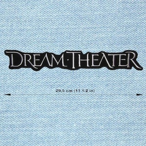 May include: A black and white Dream Theater patch, 29.5 cm long, featuring the band's name in a stylized font. The patch is rectangular with a black background and white lettering. The patch is on a light blue denim background.