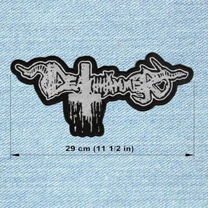Peut inclure: Un écusson noir et blanc avec le texte "DEATH WHISPER" dans une police stylisée, avec un motif de croix. L'écusson mesure 29 cm de long.