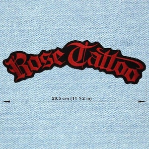 May include: A black and red embroidered patch featuring the words "Rose Tattoo" in a gothic font. The patch measures 29.5 cm (11 1/2 in) in length and is set against a light blue denim fabric.