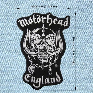 Può includere: Toppa in bianco e nero dei Motörhead, larga 19,5 cm e alta 28,5 cm, con la scritta "England" in basso. Il design presenta un teschio con zanne e catene, e il logo della band in alto.