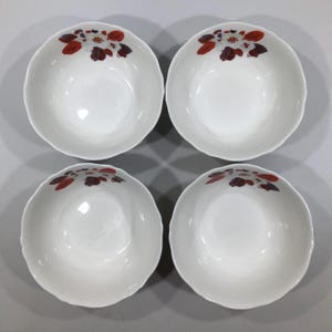 May include: Four white ceramic bowls with scalloped edges. Each bowl features a floral design in shades of red, brown, and white near the rim. The bowls are arranged in a square formation, showcasing their simple elegance.