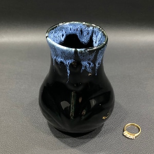 May include: A black ceramic vase with a blue and white glaze. The vase has a rounded body and a narrow neck.