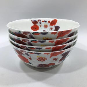 May include: A stack of four white ceramic bowls. Each bowl is decorated with a floral pattern in shades of red, purple, and green. The bowls have a scalloped rim.