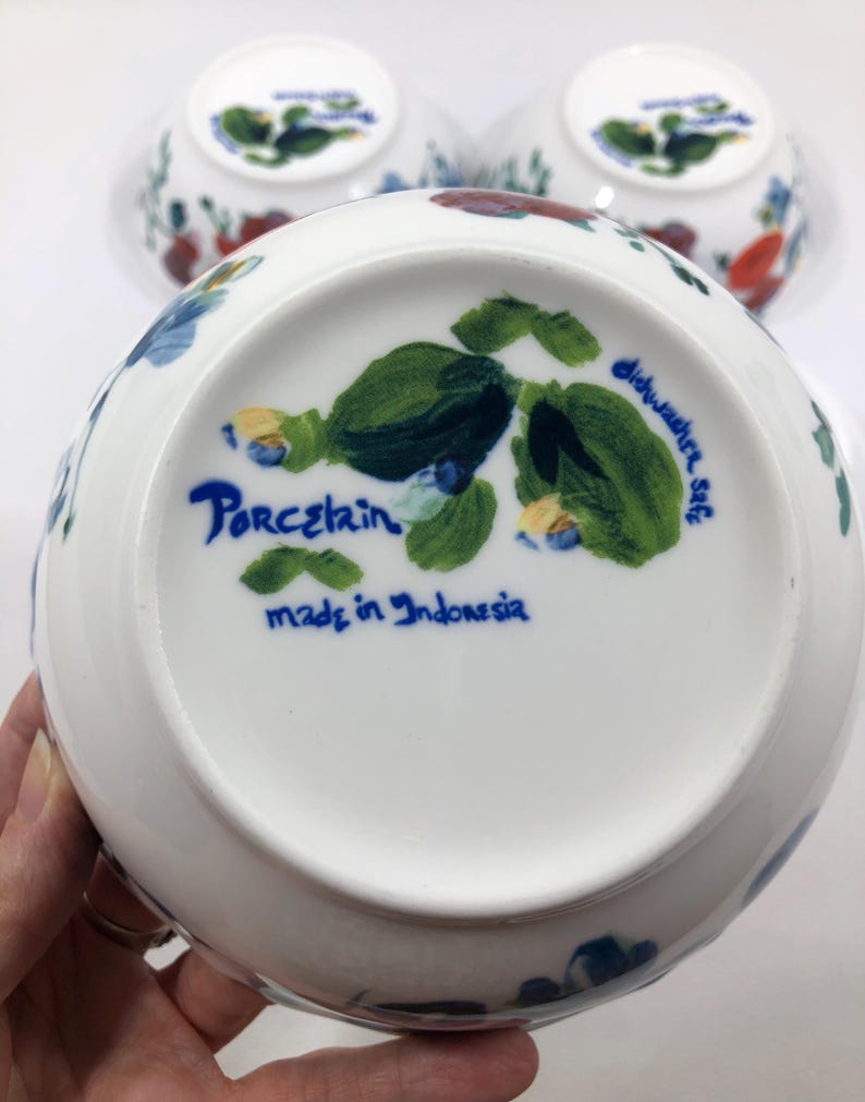May include: White porcelain bowls with floral designs in red, blue, and green. The bottom of the bowl features the words "Porcelain", "dishwasher safe", and "made in Indonesia" in blue script. Several bowls are visible.