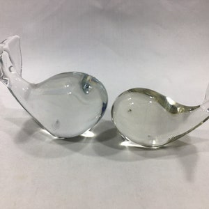May include: Two clear glass whale figurines. The whales are facing opposite directions and are made of clear glass with a slight blue tint.
