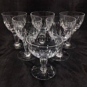 May include: Six clear glass wine glasses with a cut glass design. The glasses are arranged in a semi-circle on a black surface.
