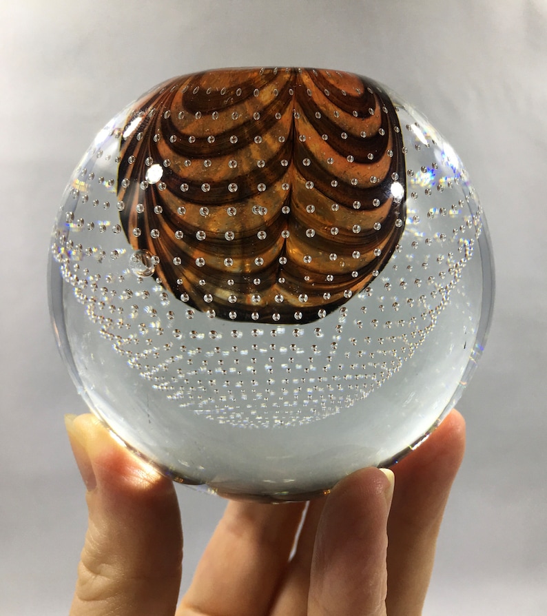 May include: A clear glass paperweight with a brown and white swirl design. The paperweight is filled with small air bubbles.