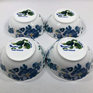 May include: Four white porcelain bowls with a blue floral design. The bowls have a rounded shape and are decorated with blue flowers and green leaves. The bottom of each bowl has the text "Porcelain made in Indonesia".