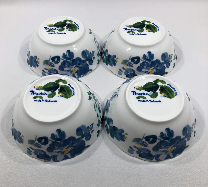 May include: Four white porcelain bowls with a blue floral design. The bowls have a rounded shape and are decorated with blue flowers and green leaves. The bottom of each bowl has the text "Porcelain made in Indonesia".