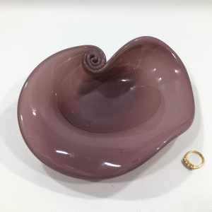 May include: A mauve glass dish with a swirl design. The dish is shallow and has a smooth, glossy finish.