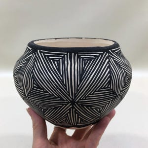 May include: A round ceramic bowl featuring a black and white geometric pattern of repeating triangles and lines. The exterior surface is covered in a dense, hand-drawn style graphic design, while the interior rim is painted with a solid black band.