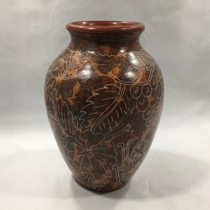 May include: A brown ceramic vase with a white floral design. The vase has a wide mouth and a rounded body. The design includes leaves, flowers, and a butterfly.