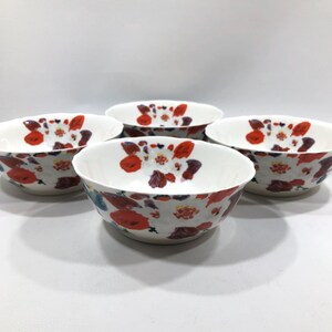 May include: Four white ceramic bowls with a floral pattern of red, purple, and blue flowers. The bowls have a scalloped edge and are arranged in a circular pattern, showcasing the design.
