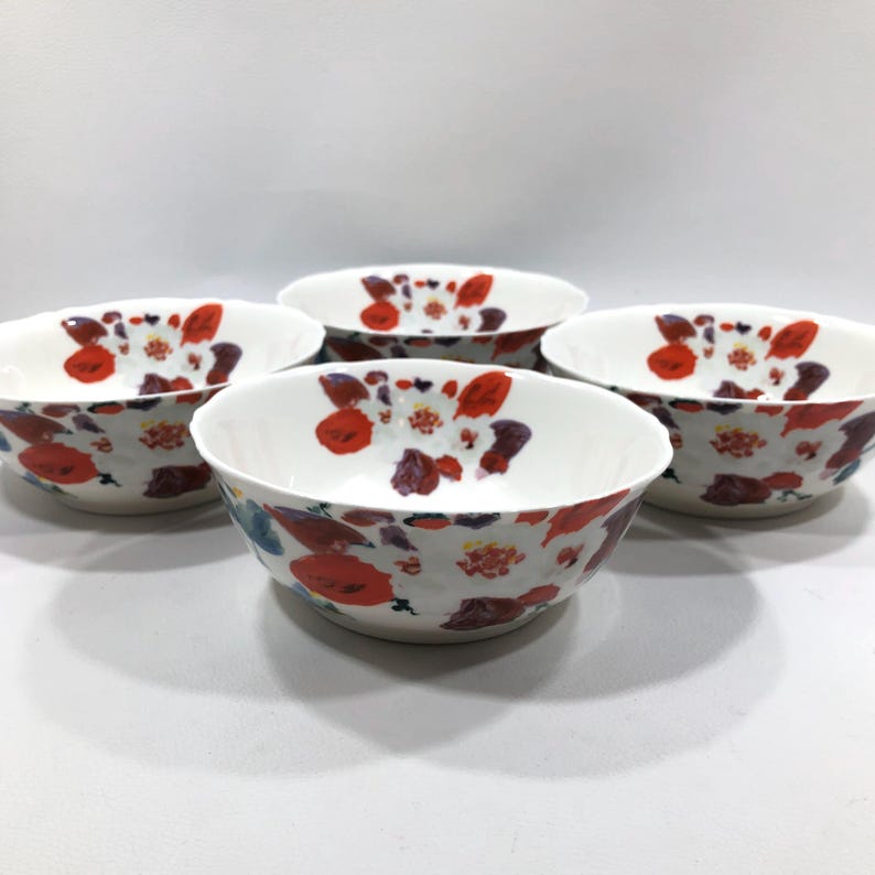 May include: Four white ceramic bowls with a floral pattern of red, purple, and blue flowers. The bowls have a scalloped edge and are arranged in a circular pattern, showcasing the design.