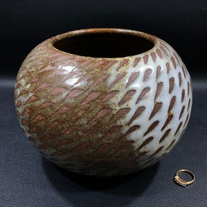 以下が含まれることがあります： 幾何学模様の茶色と白の陶器の花瓶。花瓶は口が広く、丸みを帯びたボディをしています。