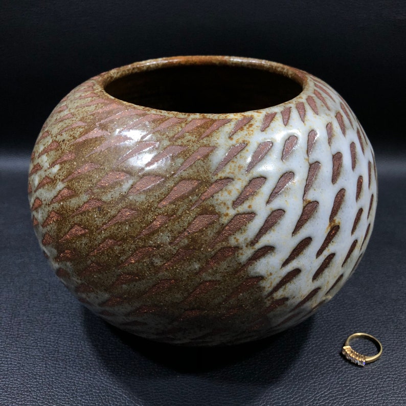 以下が含まれることがあります： 幾何学模様の茶色と白の陶器の花瓶。花瓶は口が広く、丸みを帯びたボディをしています。