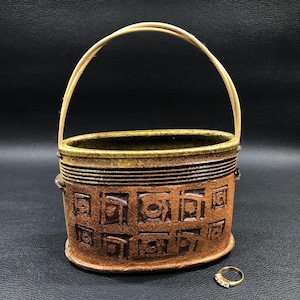 May include: A brown ceramic oval basket with a geometric pattern and a natural wood handle. The basket is sitting on a black surface.