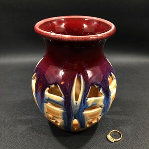 May include: A ceramic vase with a red, purple, and blue glaze. The vase has a cut-out design and is a decorative piece.