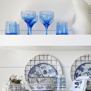 May include: A white shelf with blue and white patterned dishes, a blue and white planter with a plant, and blue glass cups and glasses.
