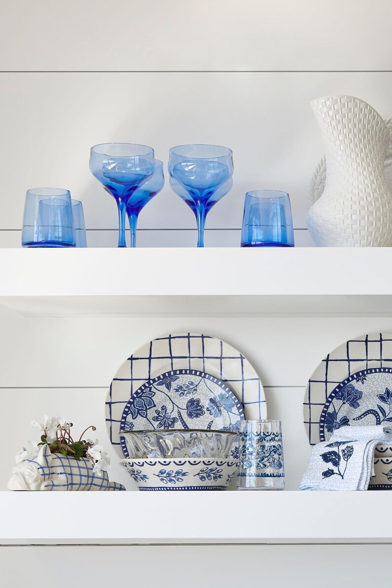 May include: A white shelf with blue and white patterned dishes, a blue and white planter with a plant, and blue glass cups and glasses.