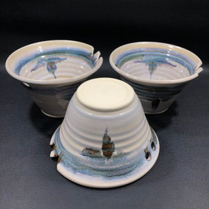 May include: Three ceramic bowls with a white glaze and blue and brown patterns. The bowls have a unique design with holes around the rim.