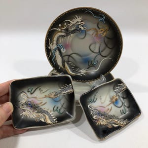 May include: Set of four black and white porcelain plates with gold accents and a dragon design. The plates are decorated with a swirling pattern and have a glossy finish.