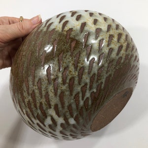 以下が含まれることがあります： 茶色と白の釉薬をかけた、大きな丸い陶器のボウル。ボウルは、小さな白い線の模様がついた、質感のある表面をしています。