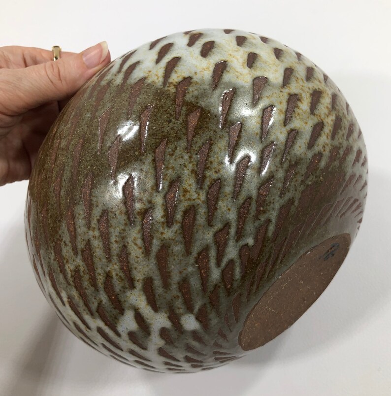 以下が含まれることがあります： 茶色と白の釉薬をかけた、大きな丸い陶器のボウル。ボウルは、小さな白い線の模様がついた、質感のある表面をしています。