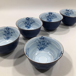 May include: Set of five blue and white ceramic bowls. Each bowl features a blue floral design and horizontal stripes on the interior. The exterior of the bowls is a solid dark blue color with a brown rim.
