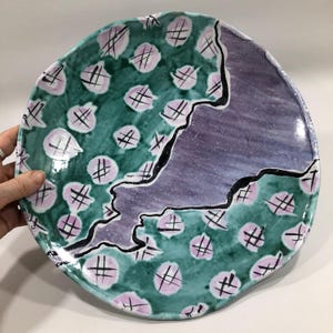 May include: A large, ceramic serving platter with a green and purple glaze. The platter has a unique, abstract design with pink polka dots and black lines.