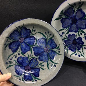 May include: Two ceramic plates with a white background and blue floral designs. The flowers are stylized and have a purple center. The plates have a blue rim.