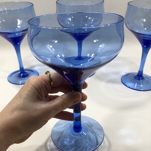 May include: Set of four cobalt blue glass wine glasses with a wide bowl and a long stem. The glasses are clear and have a slight blue tint.